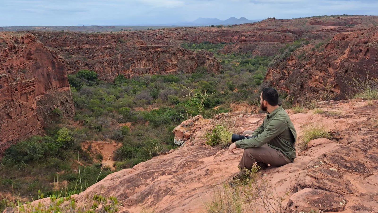 Willian Menq sentado em rocha observando canyon verdejante durante expedição