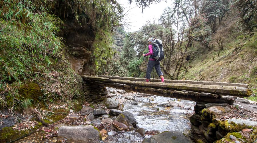 solo trekker crossing wooden river while trekking in nepal
