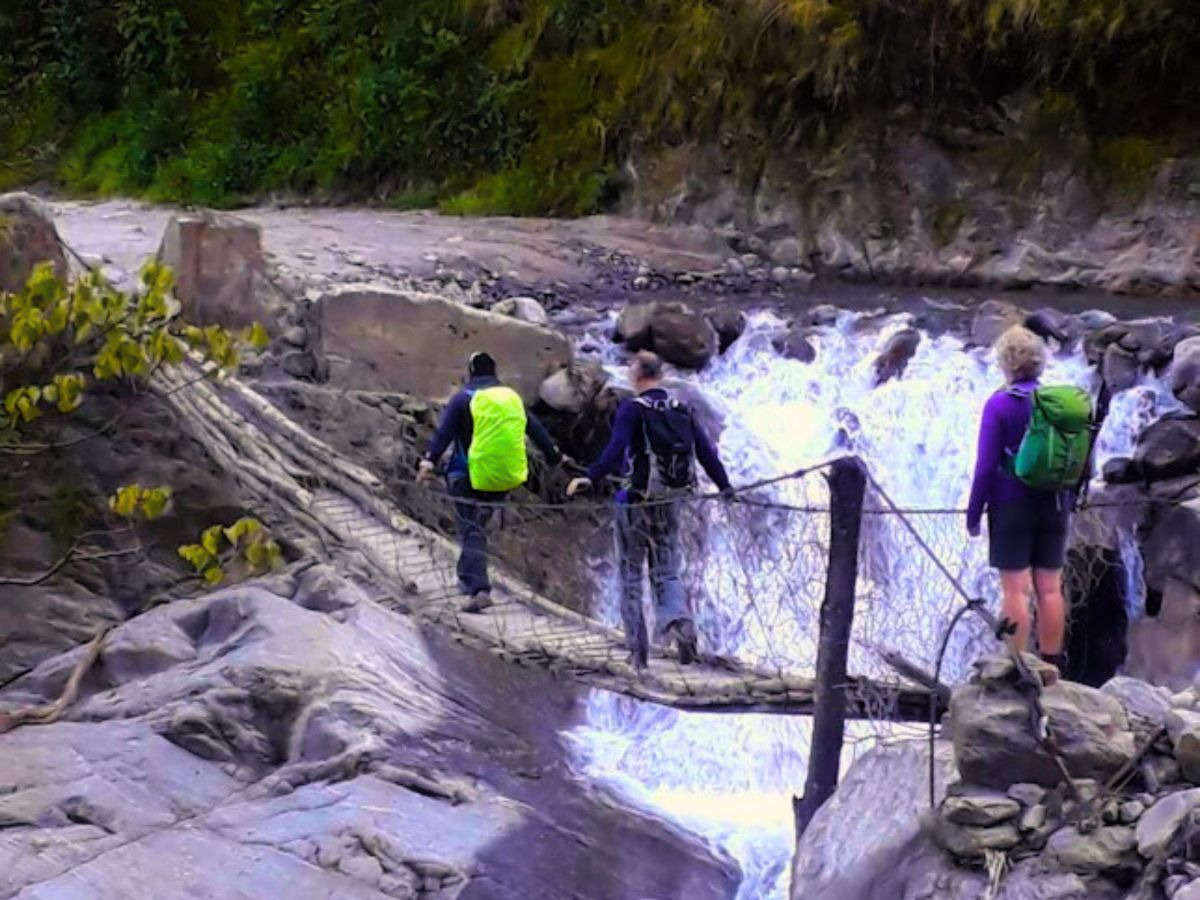 trekkers crossing wooden bridge with help of local guide in nepal
