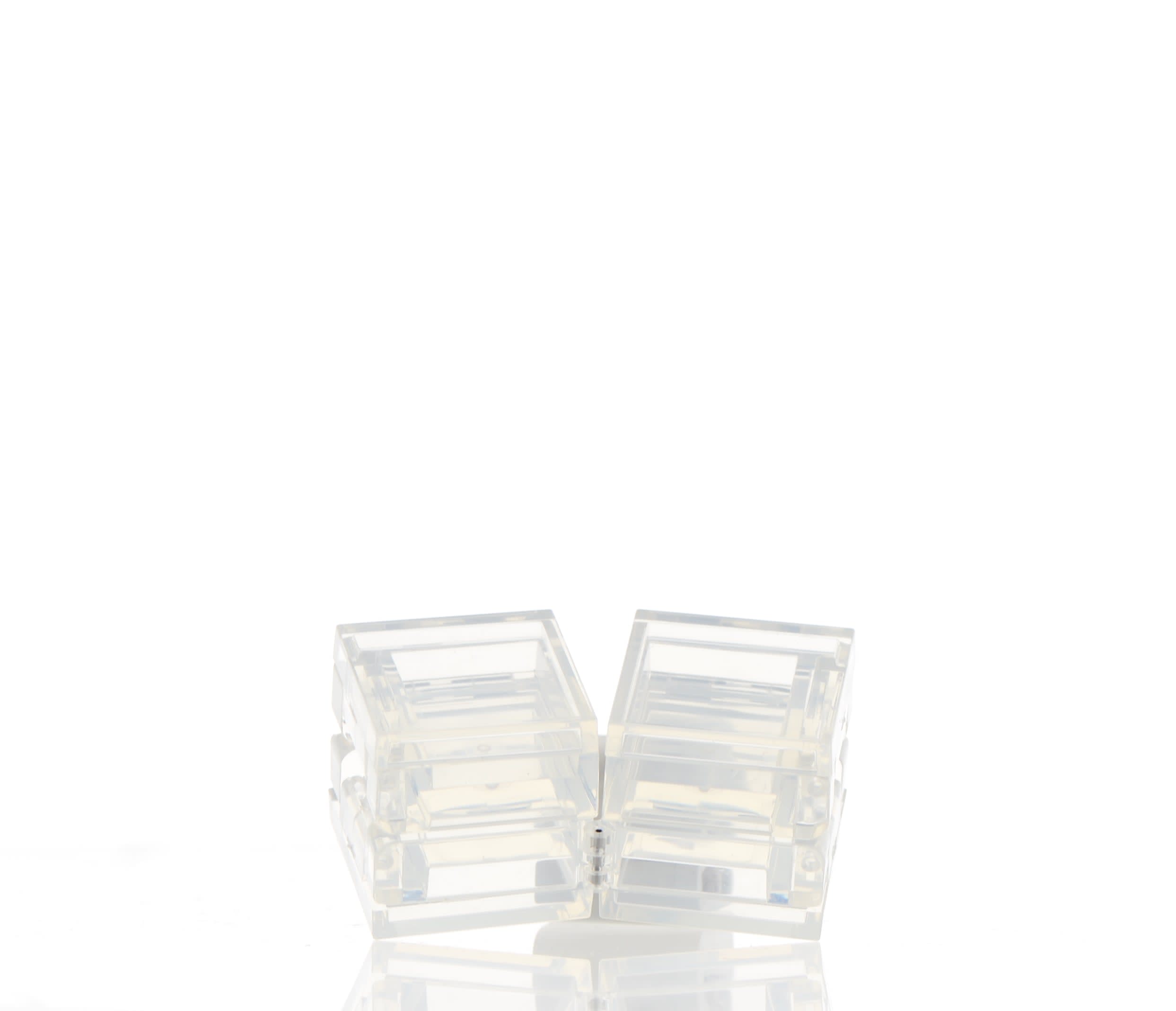 The image shows the APG Packaging 0.0oz PETG Compact (APG-400015). The compact is open, revealing a circular, empty container with a clear lid. The lid and the base are connected by a small hinge, allowing the compact to open and close. The base of the compact is slightly larger than the lid, providing a stable foundation. The clear lid allows the contents of the compact to be visible when closed. The overall design is sleek and minimalist, suitable for holding cosmetic products.