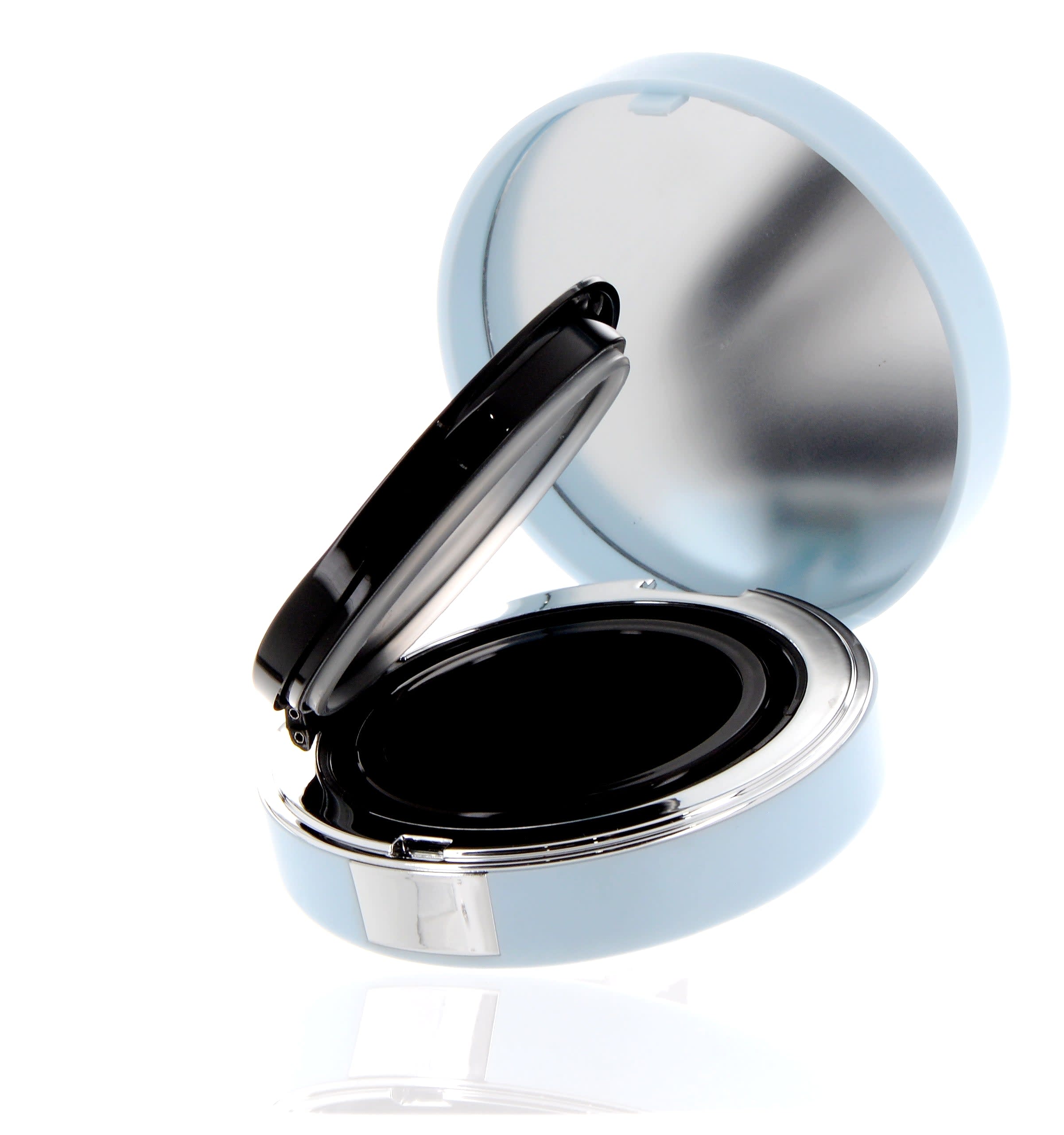 The image shows the APG Packaging 0.0oz Mixed Material Compact (APG-C503-BBS). The compact features a sleek, round design with a black exterior and a glossy finish. The top lid appears to be smooth, and the compact is slightly open, revealing a mirror on the inside of the lid. The base of the compact is also black and has a compartment that can hold makeup products like powder or blush. The overall design is minimalist and elegant.