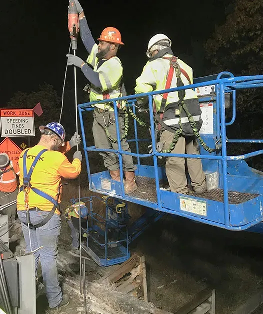 One technician on the ground helps two technicians on a construction lift