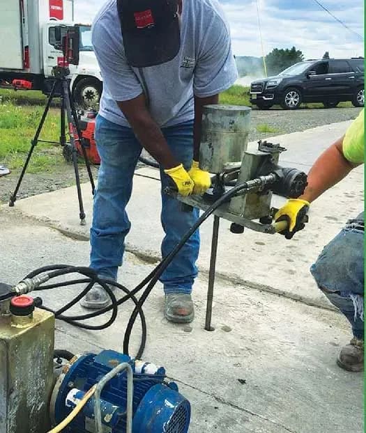 Two technicians drill hole with URETEK truck in background