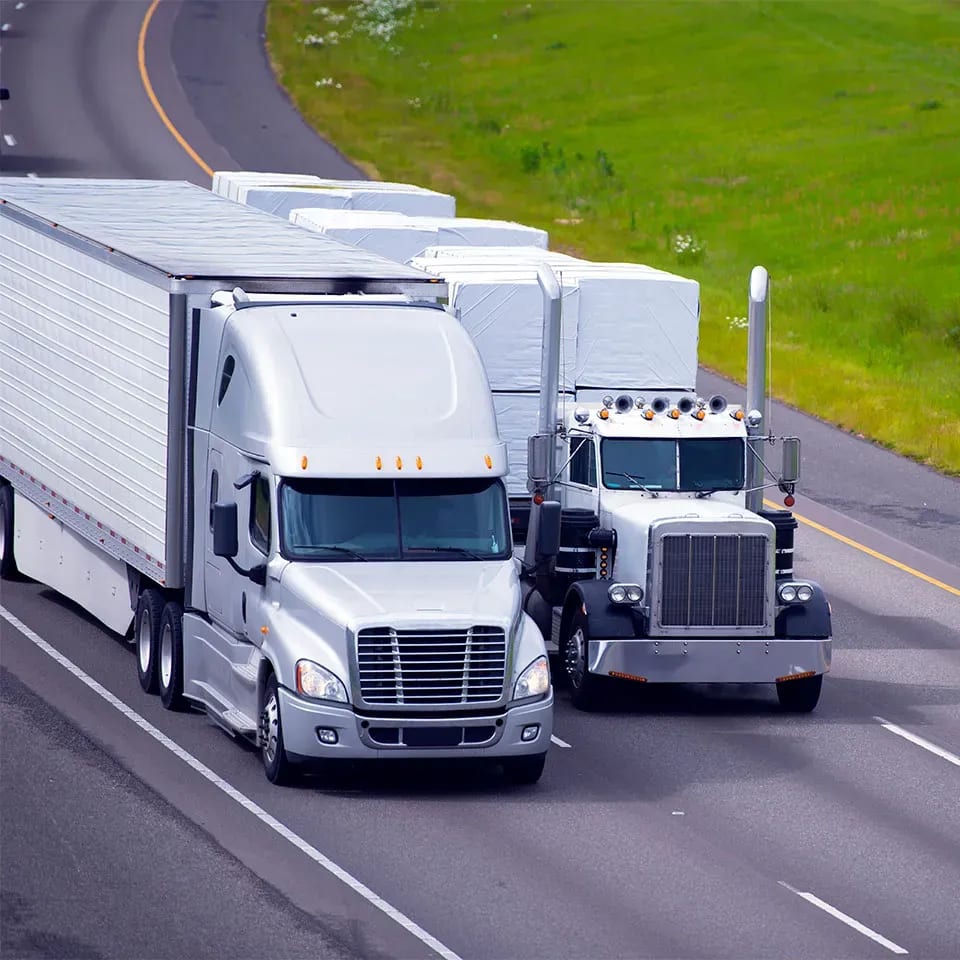 Two white semi tractor trailers driving down ighways