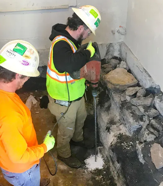 Two technicians in safety equipment work with concrete over a surface