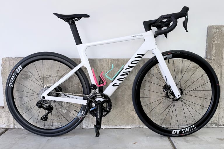 My white Canyon Endurace CF SLX 9 Di2 leaning against a concrete wall, with pink and mint bottle cages