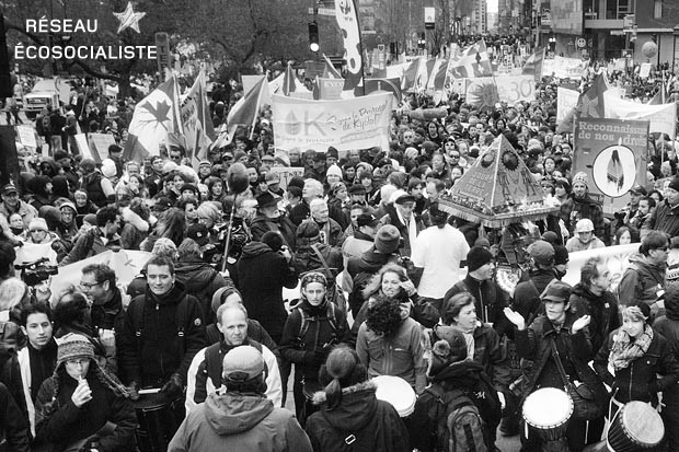 Photo noir/blanc d'une foule dense de gens manifestant sur une rue. Plusieurs bannières autochtones.