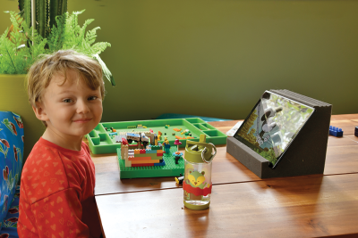 A toddler sitting at a table with Lego blocks, water bottle and Android tablet facing towards the child