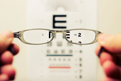 A pair of glasses holded by a man and an eye chart behind it