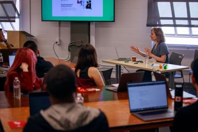 A picture of Cassie Evans seated in a workshop room explaining SVG animations to a group of smashing folks eager to learn all about the wonderful web