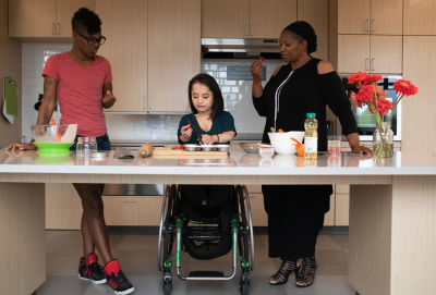 A picture of three people gathered in a kitchen preparing and tasting food