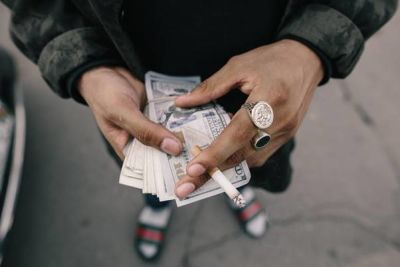 Man with rings on his fingers holding paper notes and cigarette