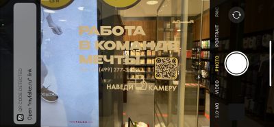 An ad shown on window glass with Cyrillic script and a QR code for customers to access the website