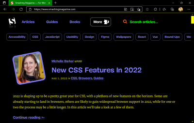 A screenshot of the Smashing Magazine homepage in Microsoft Edge. Forced Color mode is enabled, showing a stark design using neon colors on a dark background. The featured article is ‘New CSS Features In 2022’, by Michelle Barker. A photo of Michelle accompanies the headline.