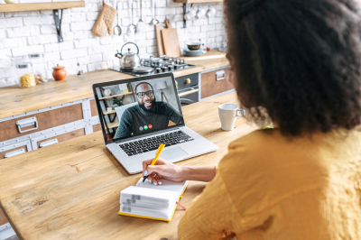 Researcher interviews a participant on a video call, writing notes as the participant answers questions