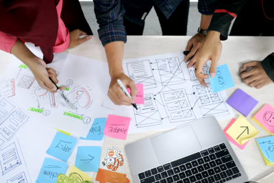 A photo with the group of people around the table with various colorful stickers and notes on it with ideas for the design of the interface.