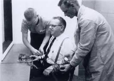 A black and white photo of two researchers attaching shock probes to a research participant