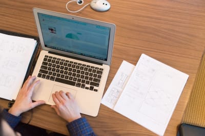 Hands at a laptop working on a website next to a sketch of some wireframes