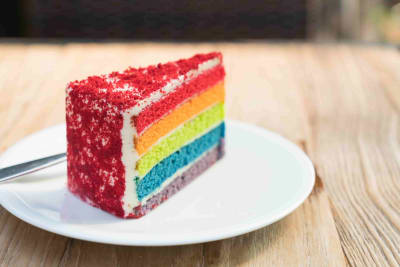 A colorful layered cake with five colors from top to bottom: red, orange, yellow, blue and purple - covered in white and red frosting