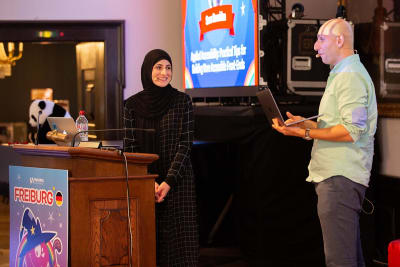 A man and woman on stage, the woman behind a lectern