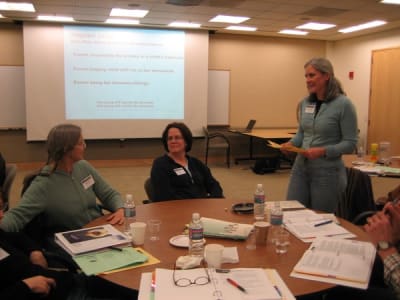 A group of people sit around a circular table reviewing training material out of notebooks