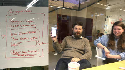 A whiteboard is showing rough sketches of a sign-up form. A man (Svein) and a woman (Ingvild) are smiling and discussing.