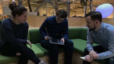 Three people in a sofa gathered around a laptop. They're discussing and smiling.