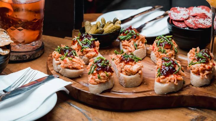 Tapas nibbles on wooden board with cocktails at Map Maison Restaurant London, stylish dining and gourmet experience