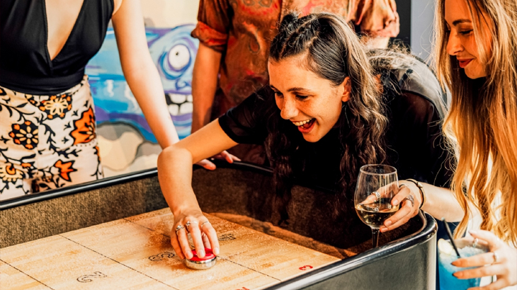 Group of friends playing shuffleboard, having fun and enjoying social games, leisure activity in London