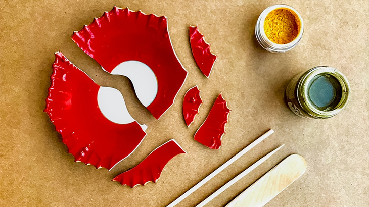 Flat lay of broken red and white plate with Kintsugi tools, resin, and gold powder
