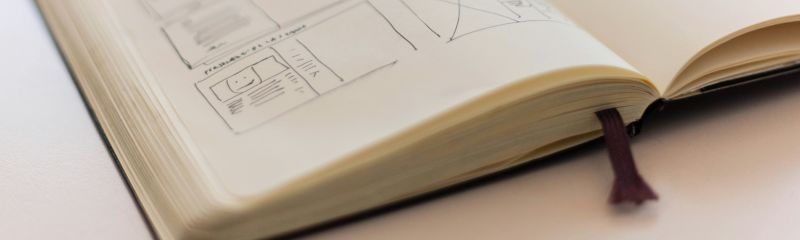 An open notebook with hand-drawn architectural sketches and diagrams lies on a desk, with a blurred background suggesting a workspace or study environment.