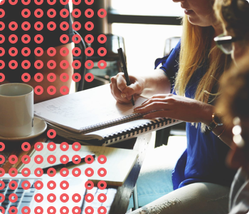 A person in a blue shirt is writing in a notebook on a table with a patterned background.