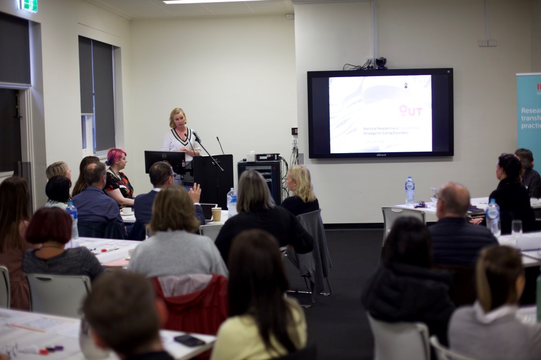A woman is speaking at a podium in front of a large audience seated in a conference room.