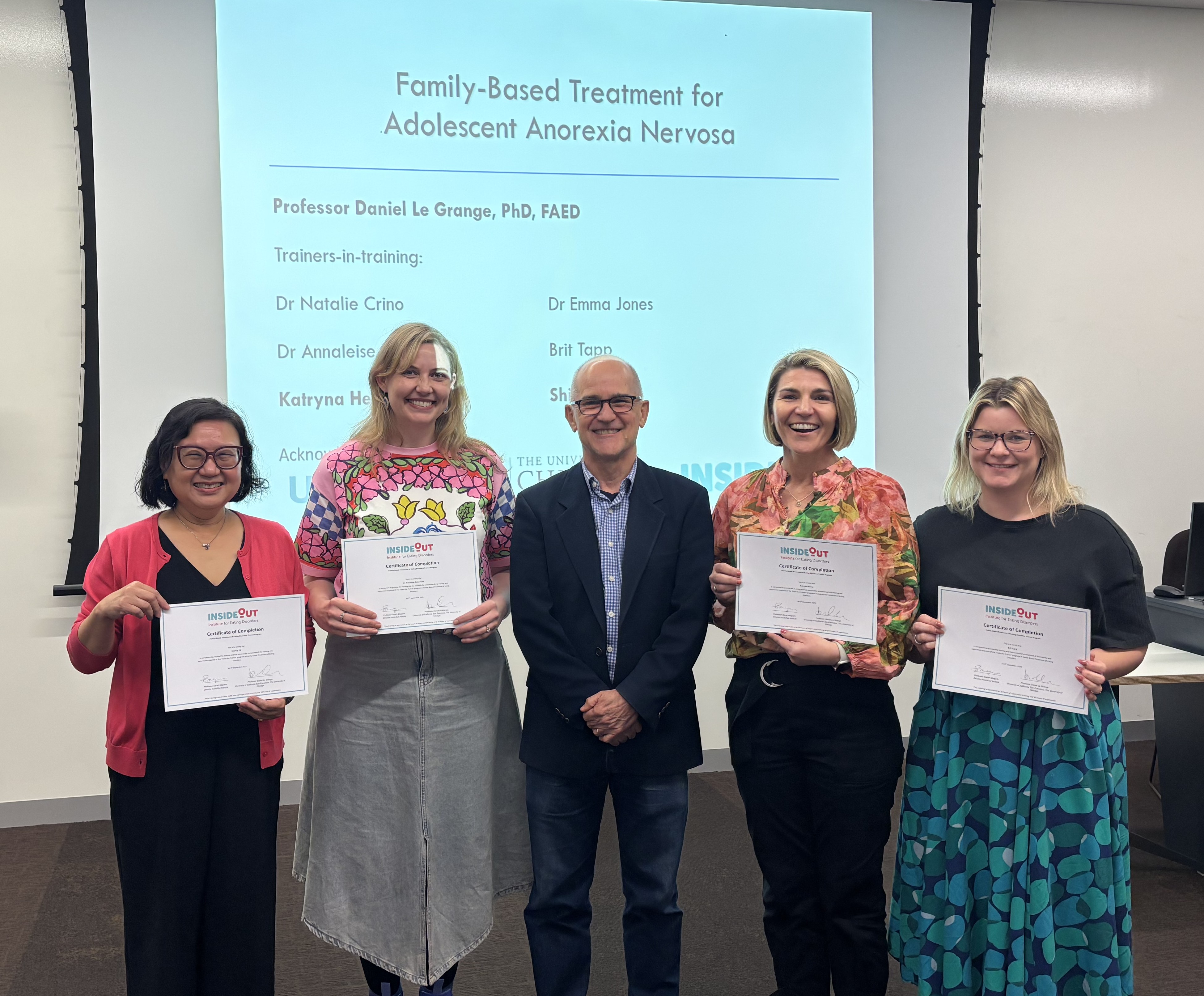 The image shows a group of five individuals, including a man and four women, standing together and holding certificates or awards.