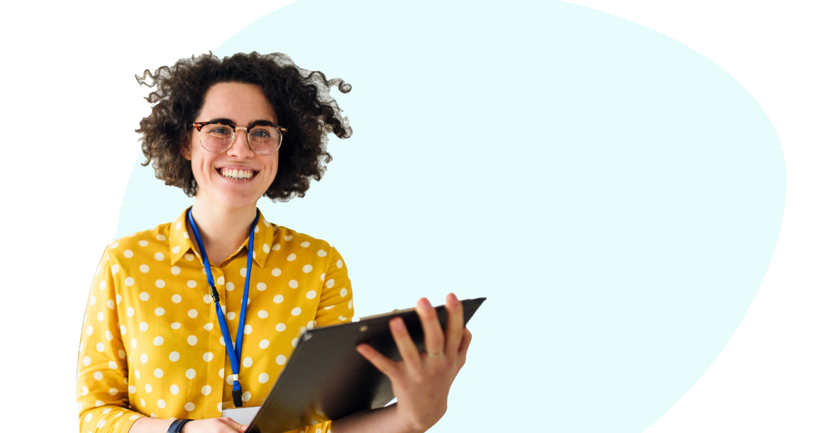 A person with curly hair wearing a yellow polka dot shirt is smiling and holding a tablet device against a light blue background.
