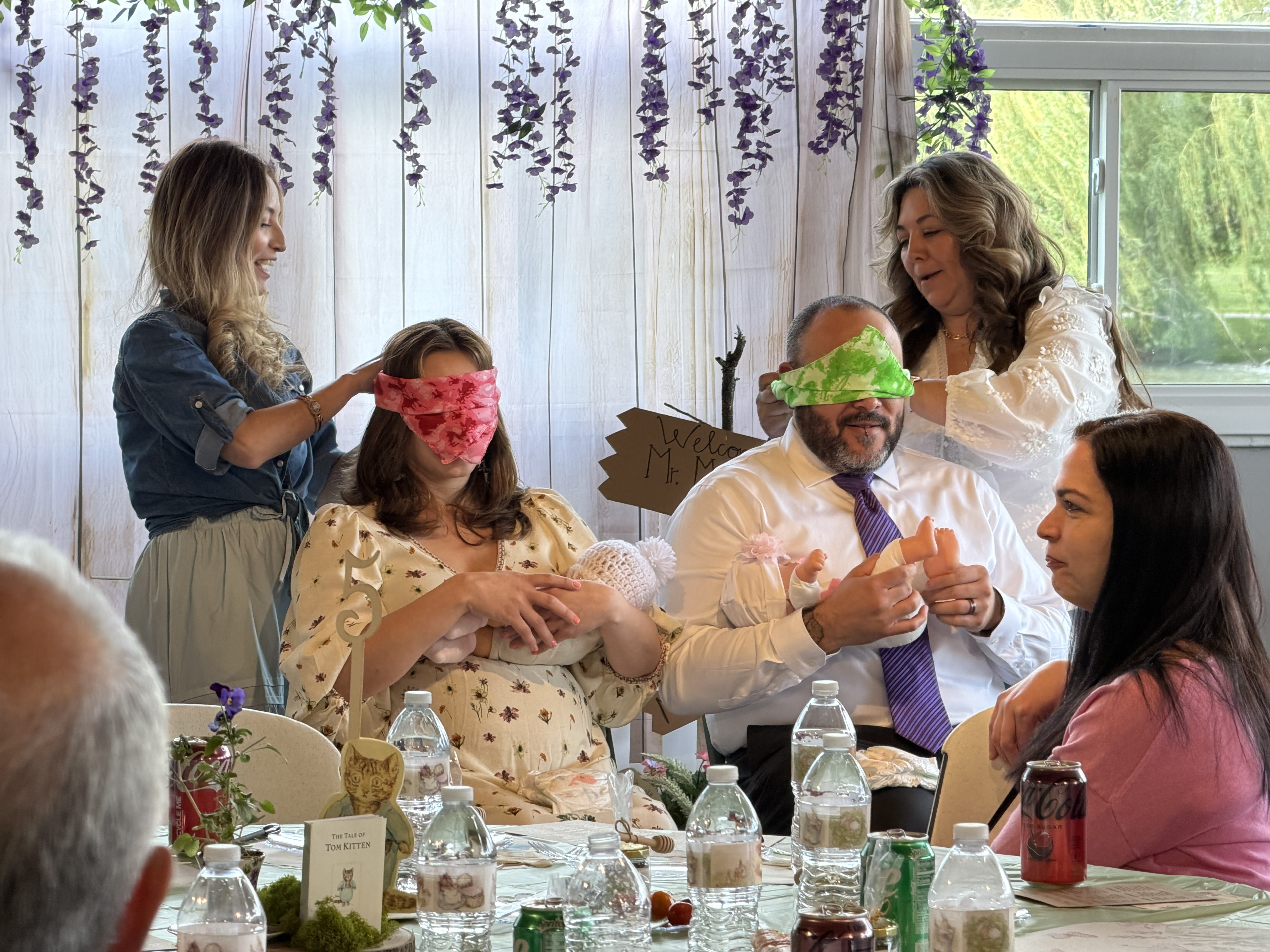 Bert and Vanessa sitting in chairs with baby dolls, trying to put diapers on them while blindfolded.