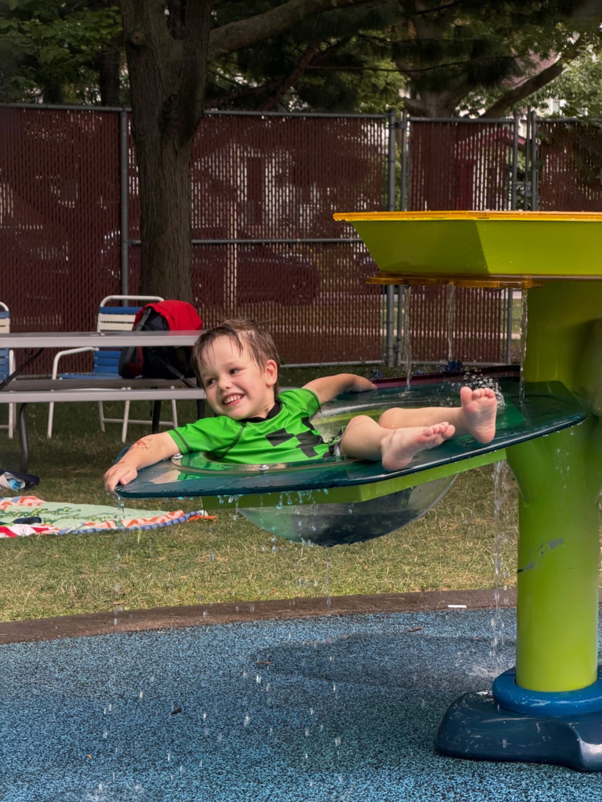 Owen sitting in what looks like a large bird bath but for kids, wearing a Minecraft swim suit.