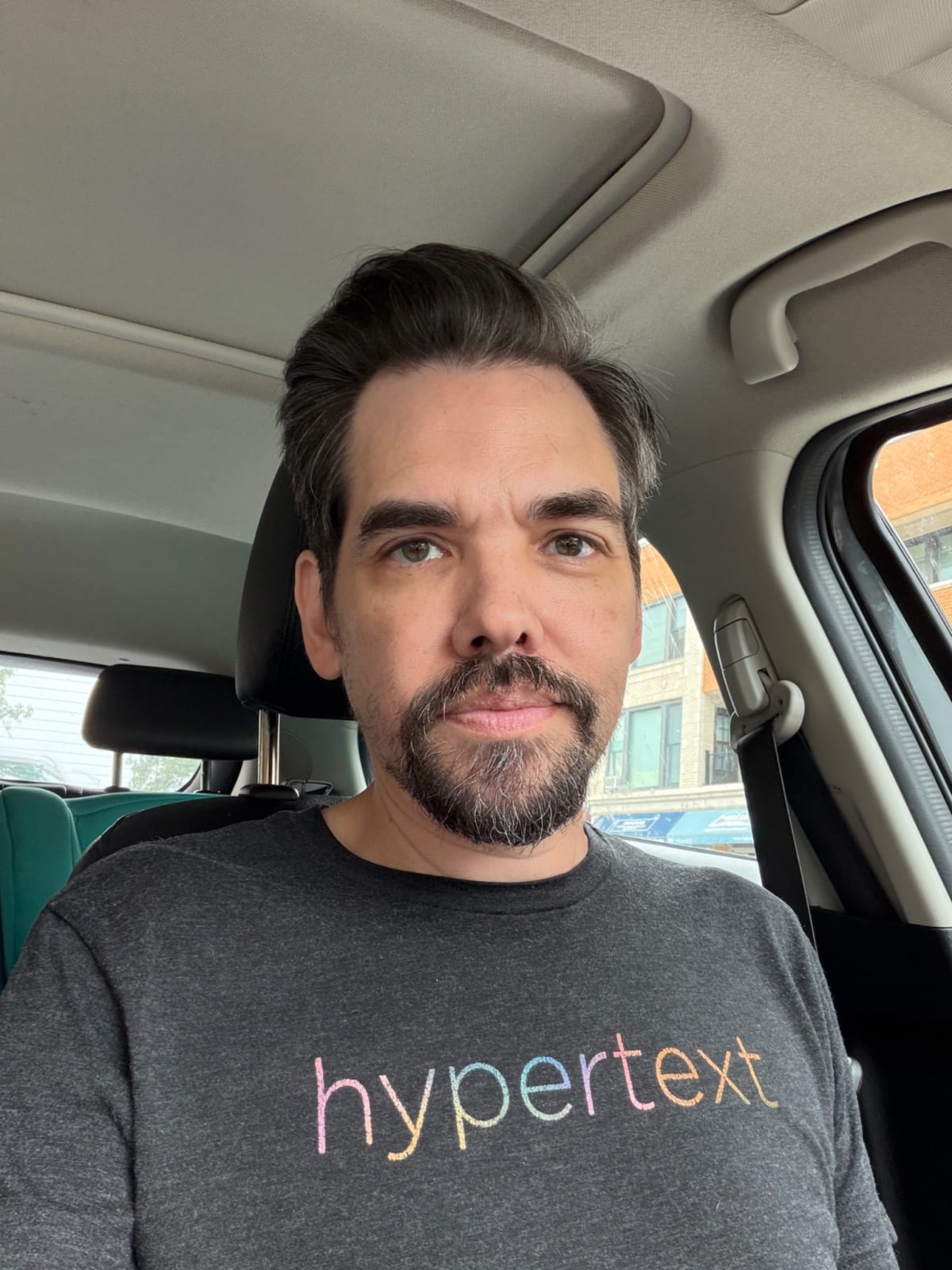 Mike in his car wearing a grey Hypertext tee shirt with a fresh haircut.