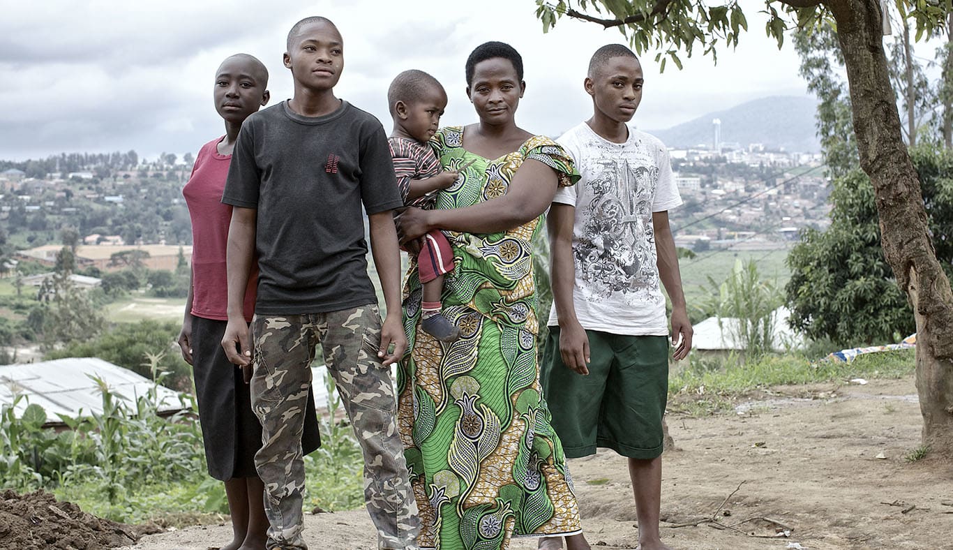 A family comprising a mum holding a baby as well as a daughter and two sons stand on a hill overlooking their town