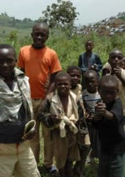 A group of children stand together in front of green hills.