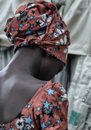 Kubili, wearing a floral dress and head scarf, photographed from the back.