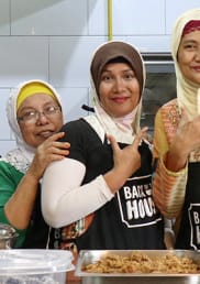 A group of smiling Filipino women gesture in front of prepared food