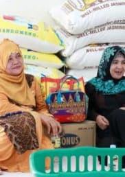 Two Filipino women smile while sitting in front of rice bags