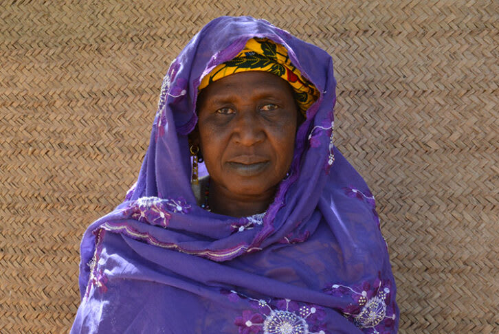 A close up of Aminatou wearing a purple shawl standing in front of a beige-coloured wall.