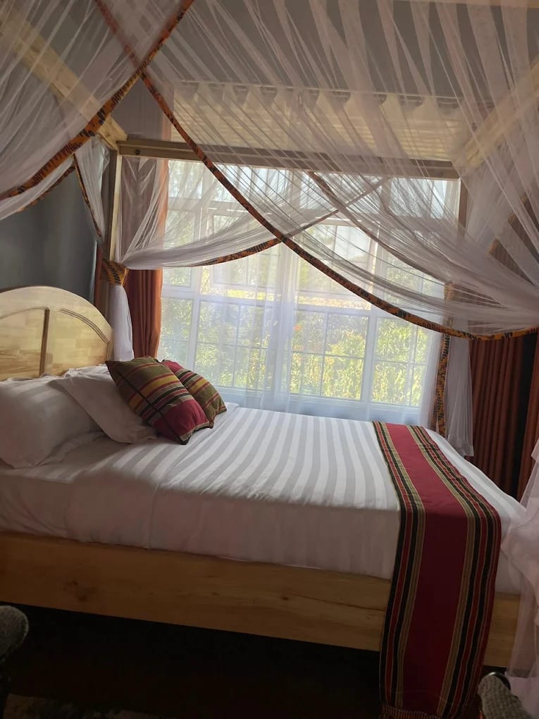 Bed with patterned cushions beside a large window with sheer curtains