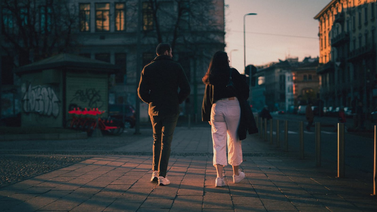 Casal caminhando devagar numa calçada ao entardecer.
