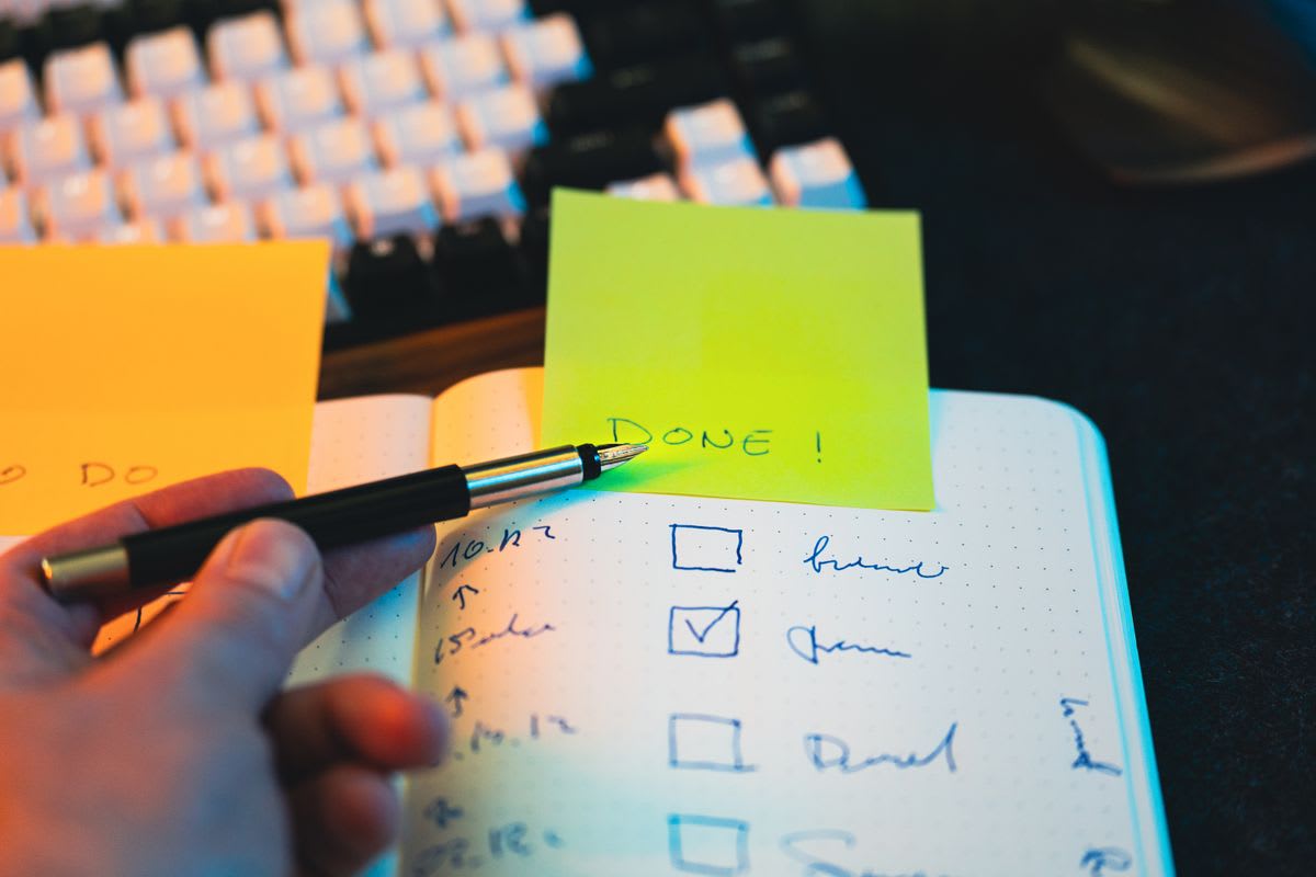 Caderno com lista de tarefas marcadas e um post-it escrito "DONE!"
