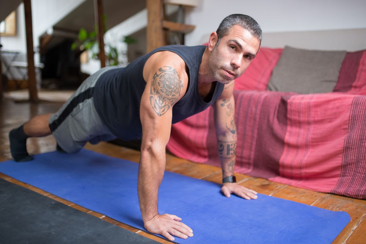 Homem fazendo flexão de braço em um tapete de exercício na sala de casa