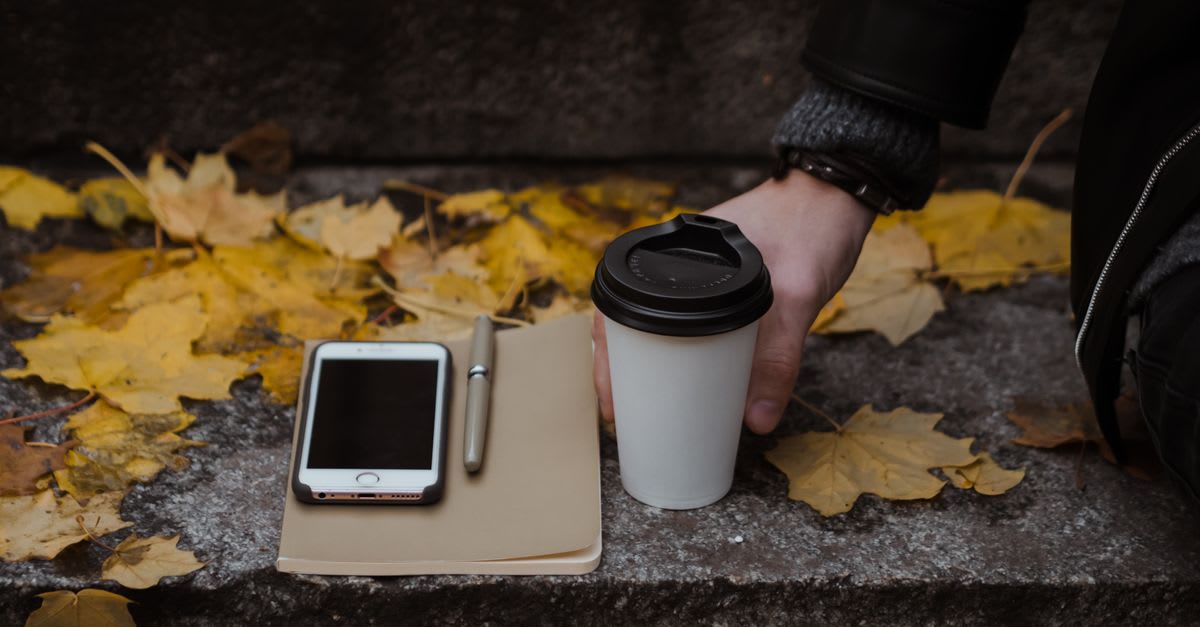 Caderno, café e celular sobre uma superfície com folhas