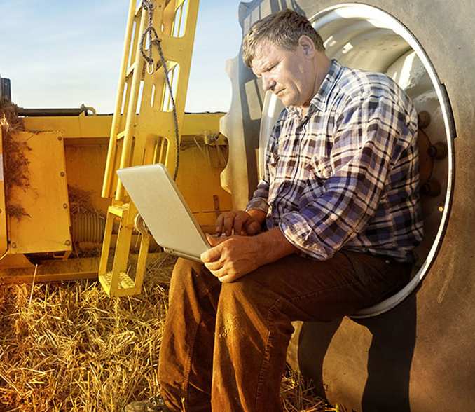 Kmetovalec na traktorju s prenosnikom v rokah